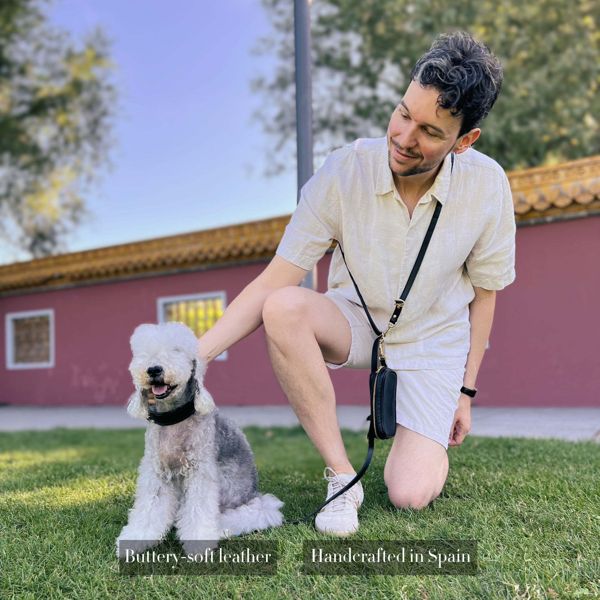 Man kneeling on grass with a dog, wearing a handsfree dog leash in crossbody mode with a pouch for treats, made from soft black leather. #lang_en