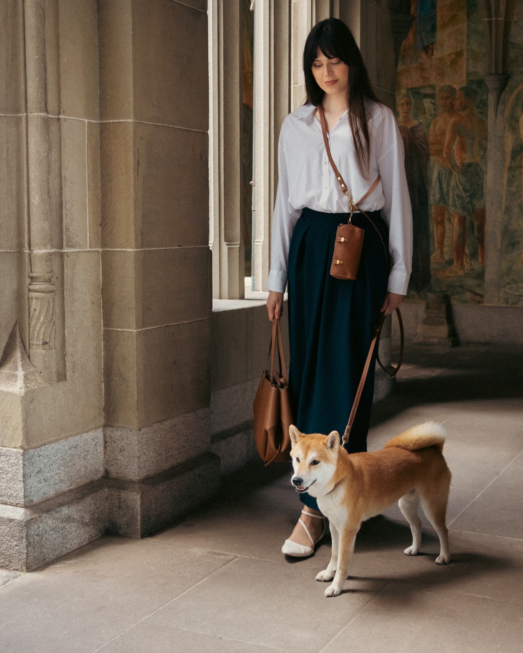Woman walking a dog in an architectural setting with columns and artwork.