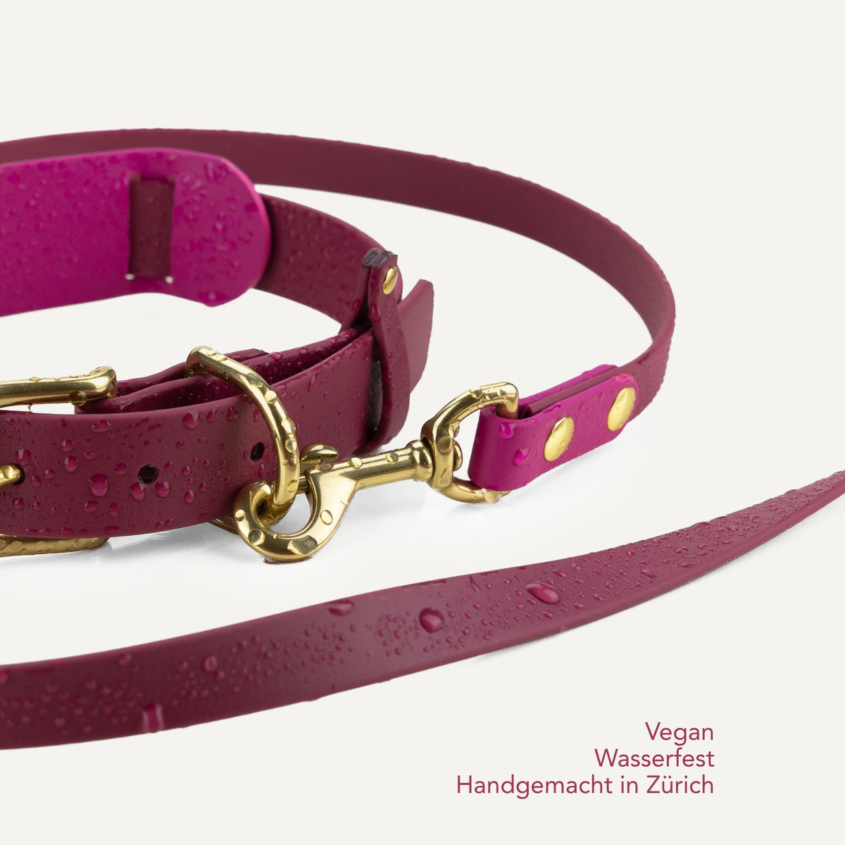 A close-up of a magenta vegan leather dog collar and matching leash with gold-tone hardware, shown on a light off-white background with water droplets on the surface. Text in the bottom right corner reads 'Vegan Waterproof Handmade in Zürich'. #lang_de