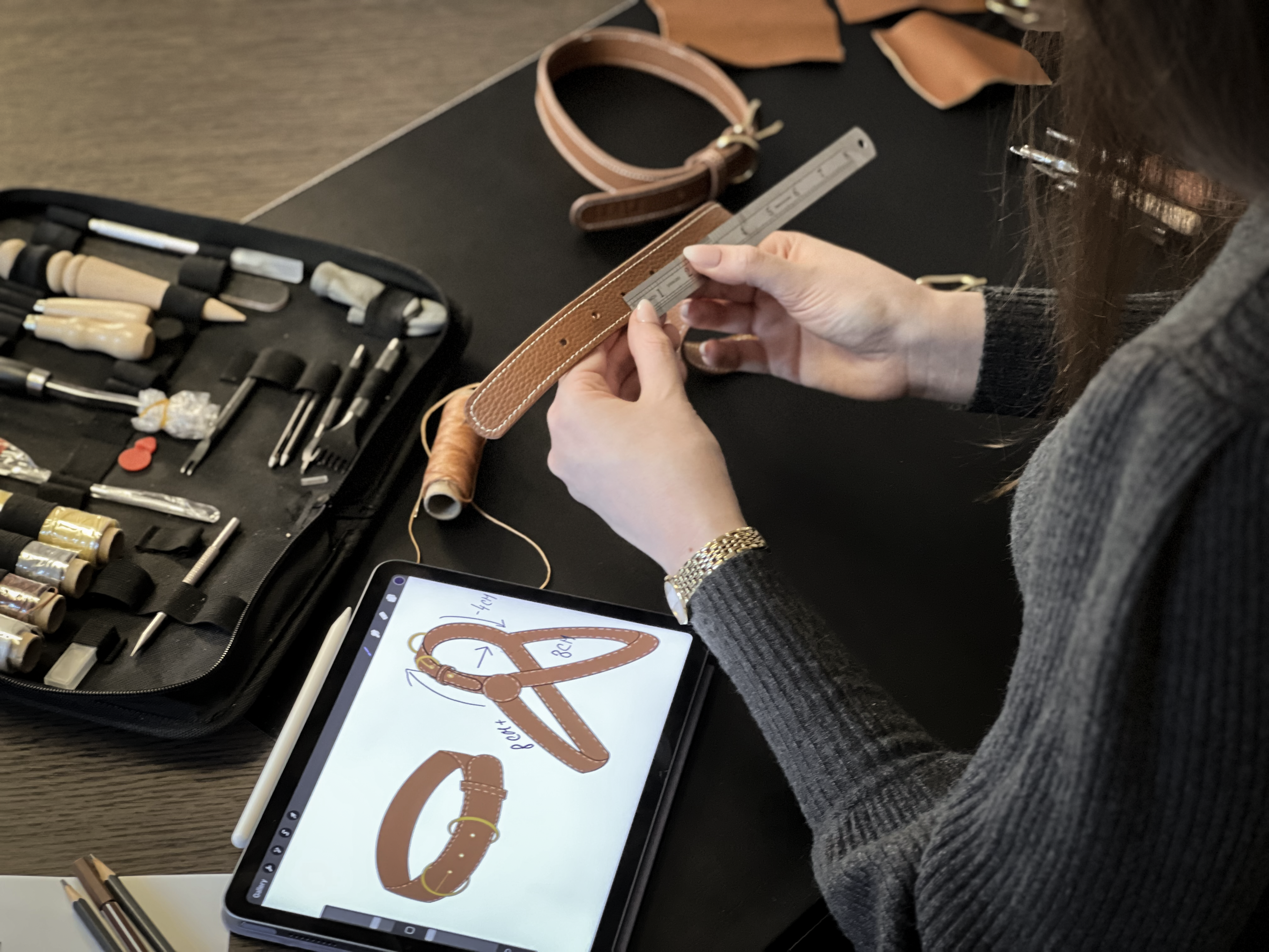 Closeup picture of a woman sitting at her desk working on leather products for dogs with tools and a tablet