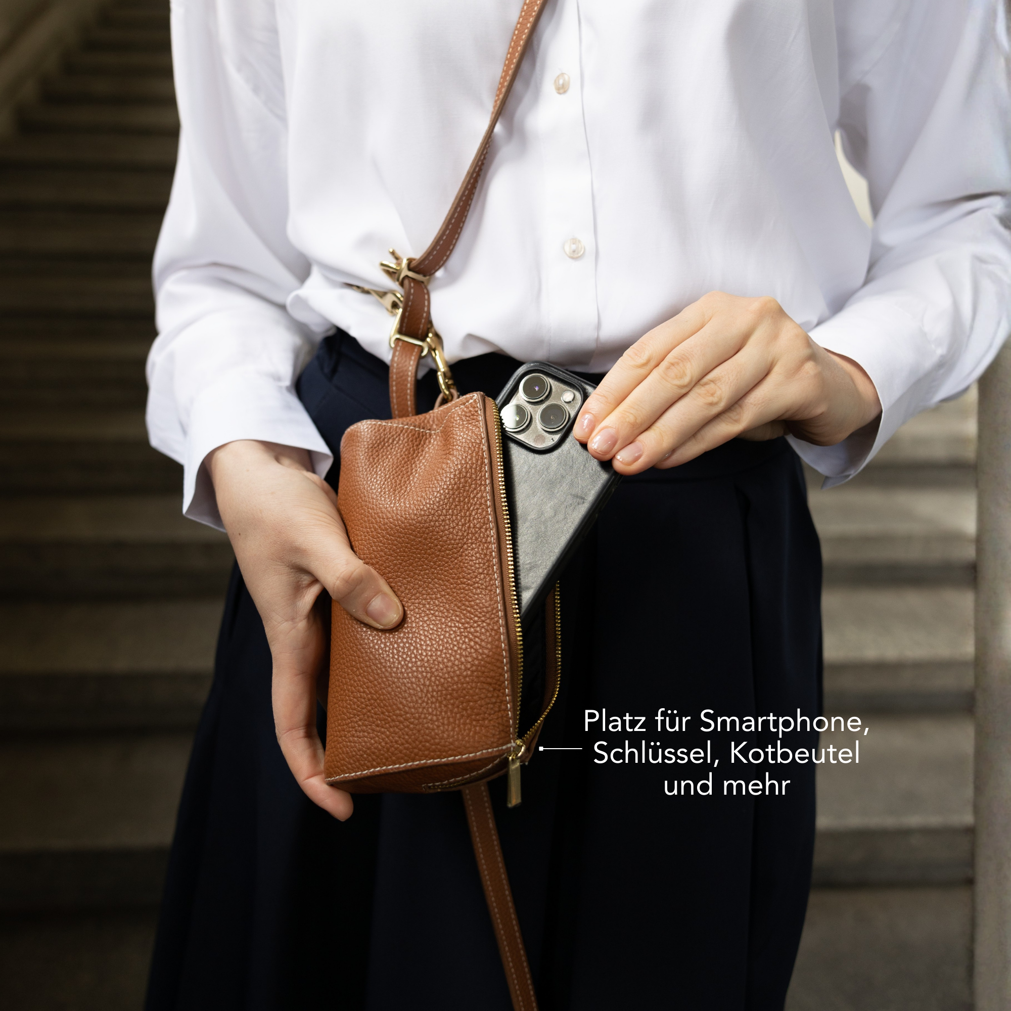 Person holding a brown leather crossbody bag with text in German. #lang_de